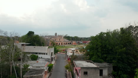 Forwards-fly-above-street-in-town.-Revealing-park-and-old-brick-building-of-Convent-of-San-Bernardino-de-Siena.-Historic-landmark.-Valladolid,-Mexico