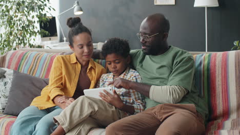 familia afroamericana alegre usando una tableta digital en el sofá en casa