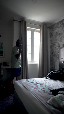 un anciano del sur de asia haciendo una llamada telefónica mientras está de pie junto a la ventana en una habitación de hotel, disfrutando de un momento de comunicación tranquila.