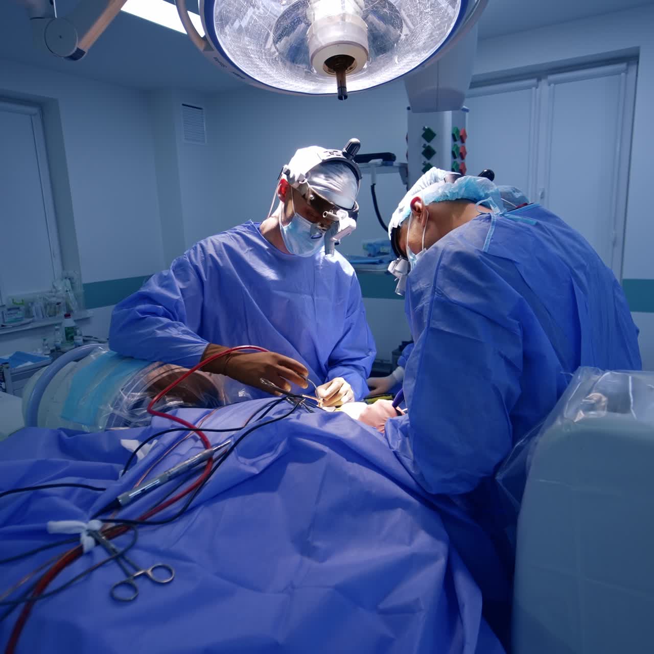 Big modern surgical room with diverse technological equipment. Two surgeons cooperate performing neurosurgery
