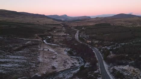 Kurvenreiche-Straße-Durch-Eine-Zerklüftete-Landschaft-In-Der-Abenddämmerung,-Skye,-Luftaufnahme