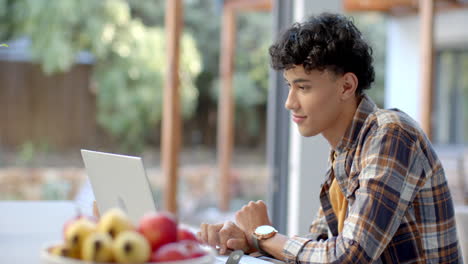 using laptop, young teenage boy sitting at table with fruit bowl, working from home