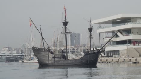 Ferdinand-Magellan-Nao-Victoria-carrack-boat-replica-with-spanish-flag-being-docked-in-Valencia-with-veles-e-vents-in-the-background-in-slow-motion-60fps