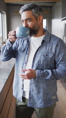 video vertical de un hombre biracial sosteniendo una taza de café en la cocina