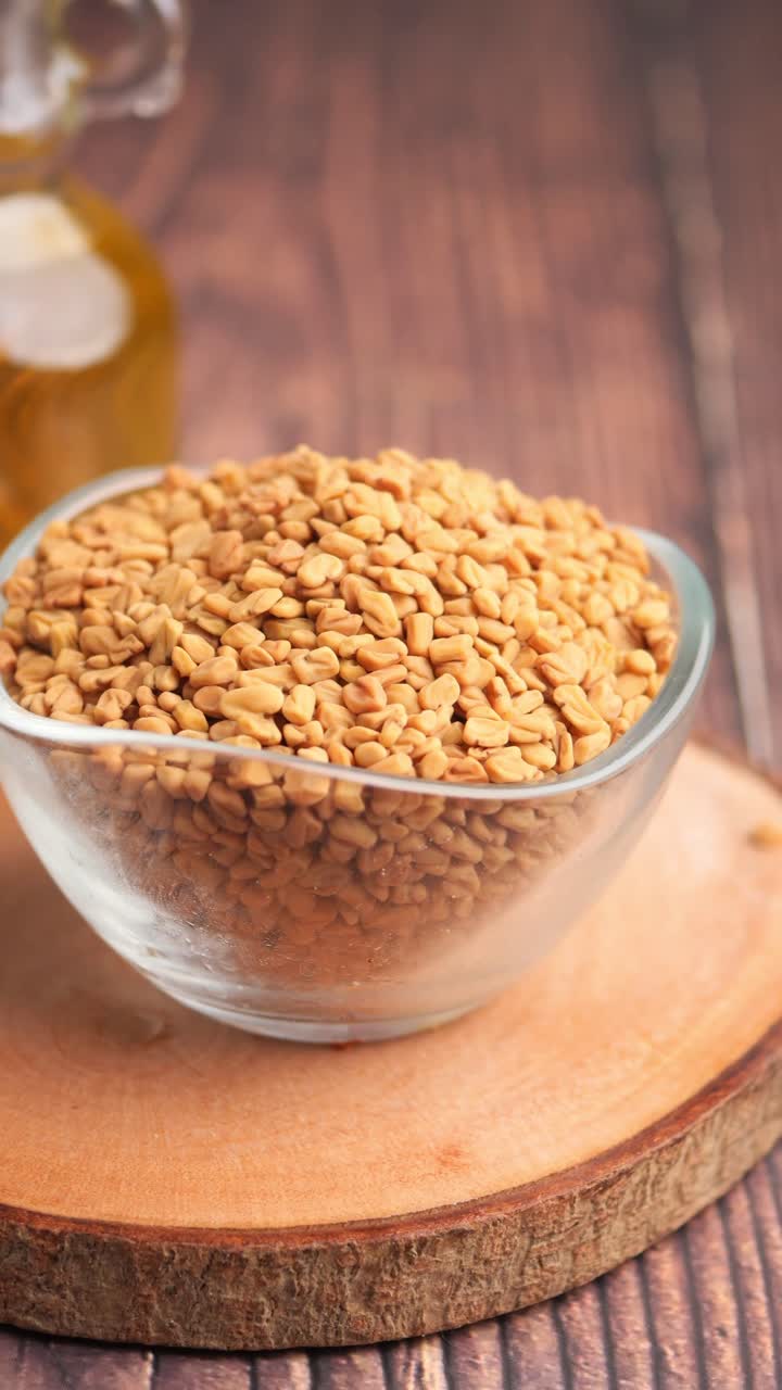 Semi di fieno greco in ciotola di vetro con olio su sfondo di legno