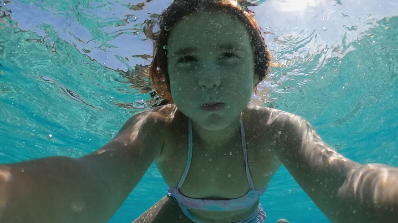 underwater selfie of pretty little red-haired girl holding breath while  immersing in transparent sea water