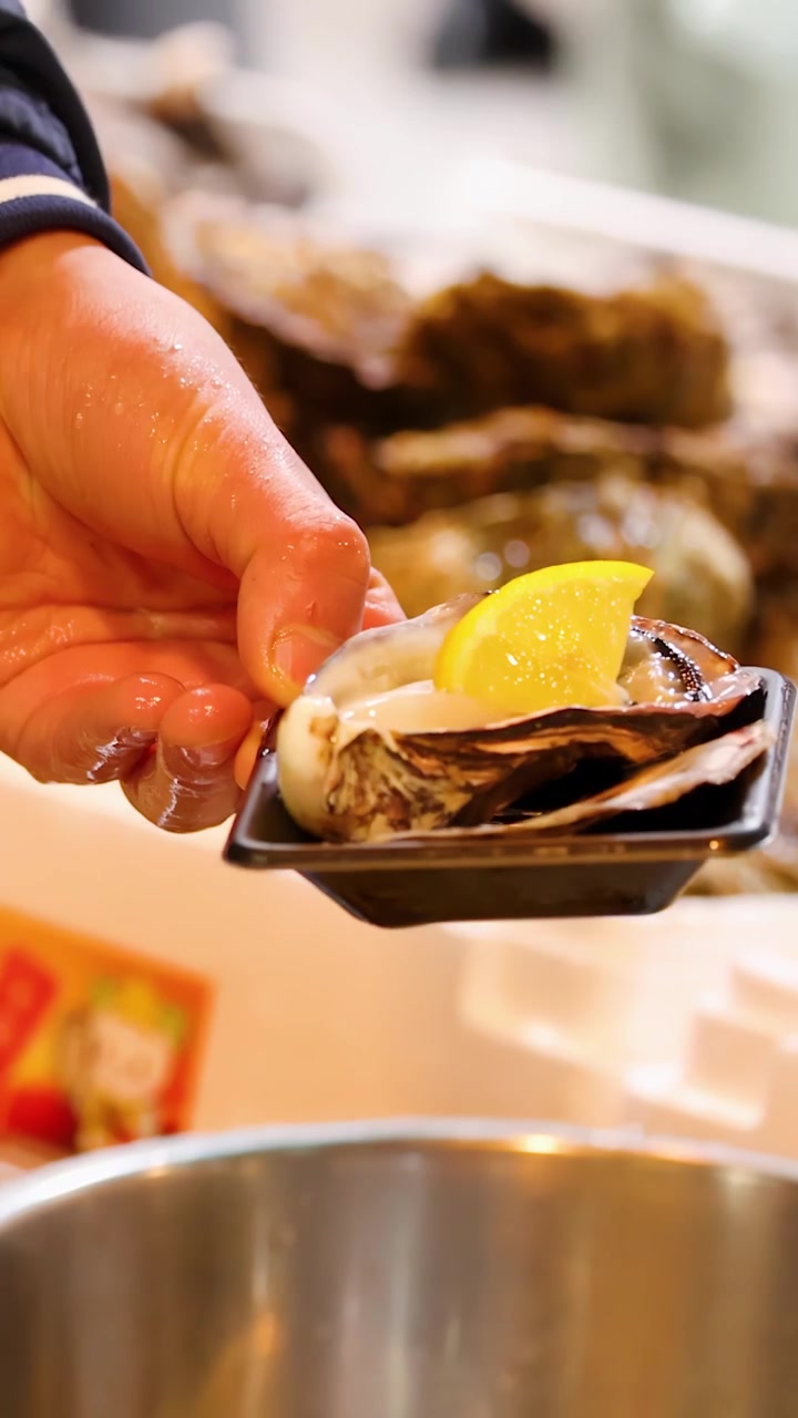 Close-up of a vendor preparing fresh raw oysters with lemon at Tsukiji Market, Tokyo.