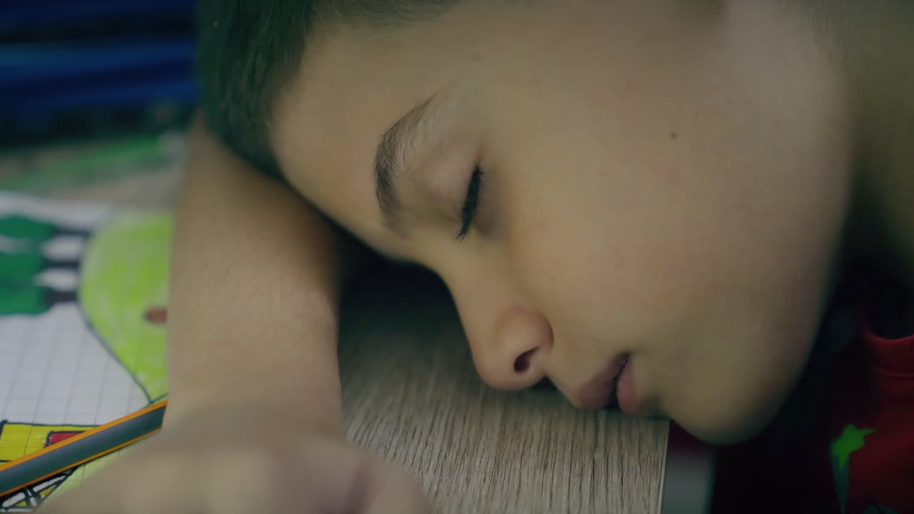 niño cansado hace la tarea por la noche y duerme en el escritorio