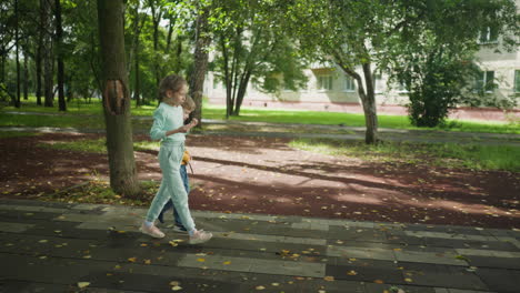 children seen heading home along paved path with tree in foreground and residential building in background, soft natural light filters through branches, casting shadows on moist ground