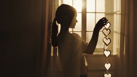 silhouette of a girl holding heart decorations in front of a sunlit window