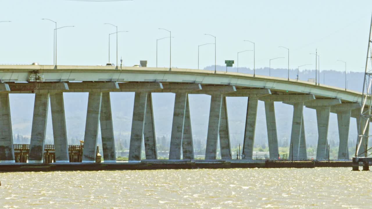 Cars and trucks crossing Dumbarton bridge form a low point showing the concrete supports in the bay area of San Francisco