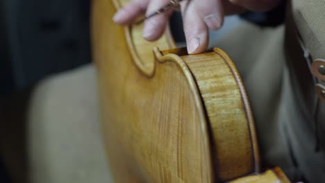 detailed view of a violin maker applying dark pigment to the ribs of a violin during the antiquing process, enhancing texture and simulating natural wear to achieve a convincingly aged appearance