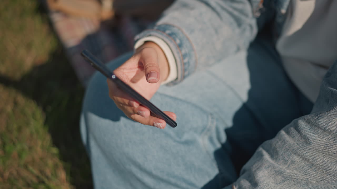 Relaxing outdoor smartphone usage. Relaxing moment with phone and notifications outdoors in nature. Casual leisure scene showing person scrolling on phone during picnic in grassy environment