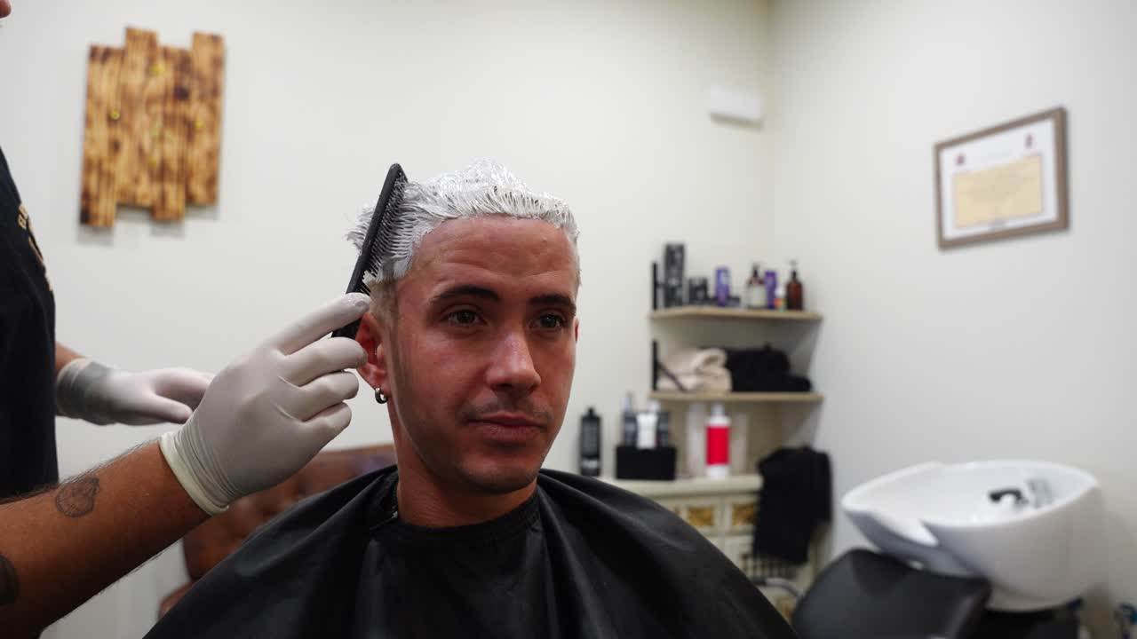 Close-up of hairdresser using a comb to test bleaching powder dryness on client’s hair as they laugh