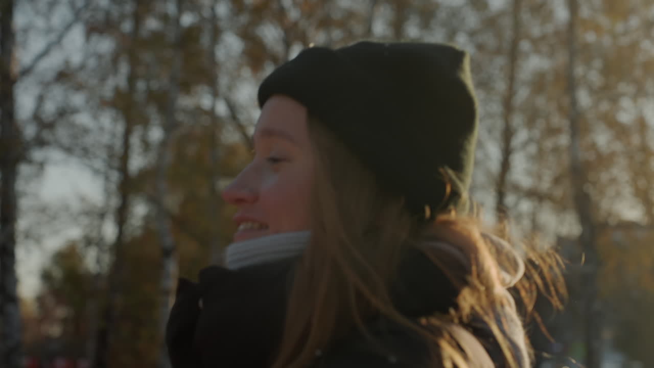 Backlit Caucasian woman walking autumn park holding plush rabbit, wearing beanie and backpack golden late afternoon light filters through birch trees candid profile shots capture warm smile, bundled