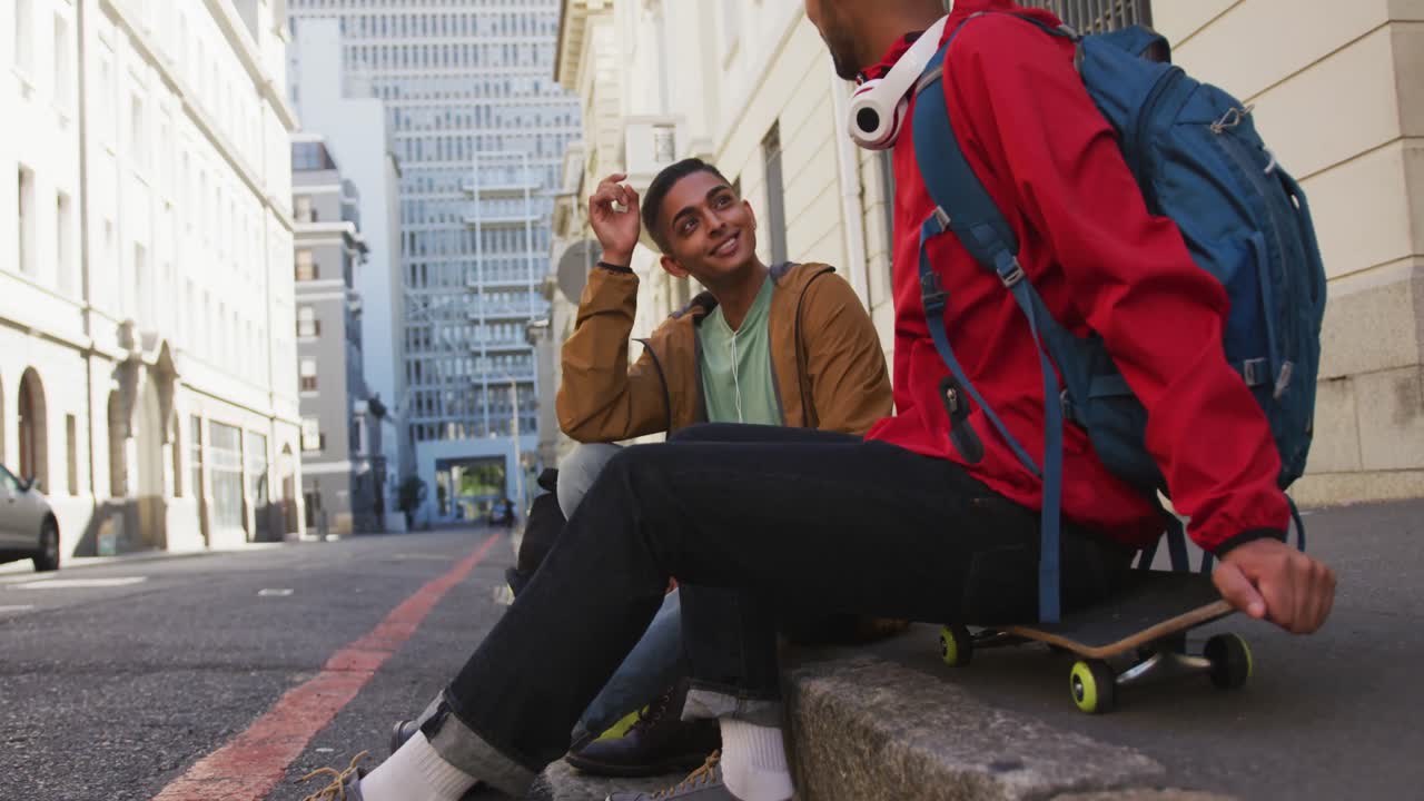 dos felices amigos de raza mixta sentados y hablando en la calle