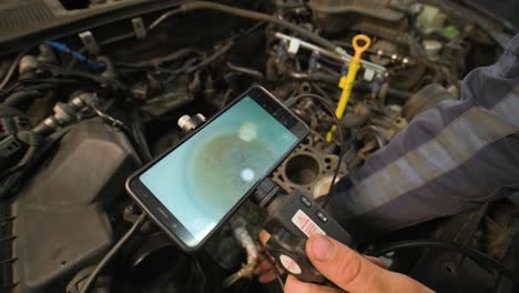 hands of car mechanic check the vehicle engine with technical endoscope with rotary camera and mobile phone. repair of engine head and valves.