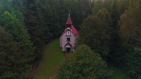 drone shot of a remote chapel in the middle of forest in the cloudy evening in lithuania