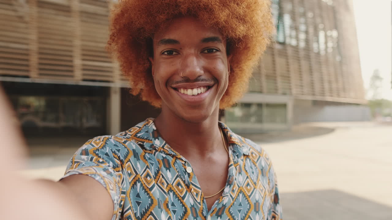Giovane uomo allegro con capelli ricci in posa per un selfie all'aperto.