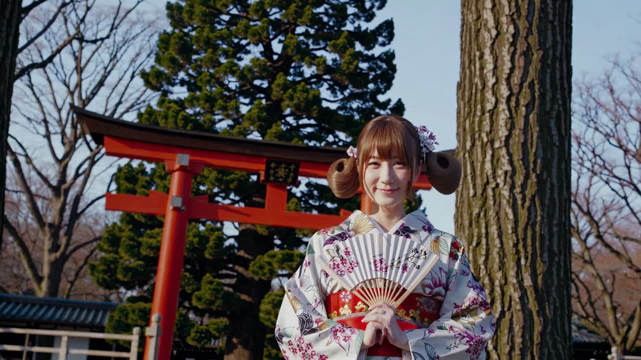 Un fotogramma di un video di una donna con un kimono a fiori che tiene in mano un ventaglio, ripresa da un angolo frontale