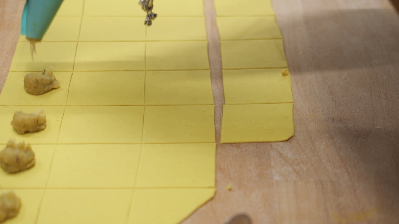 Professional chef preparing fresh tortelli fresh pasta dough at a wooden counter, using a piping bag to stuff ravioli in traditional Italian cuisine in a restaurant kitchen