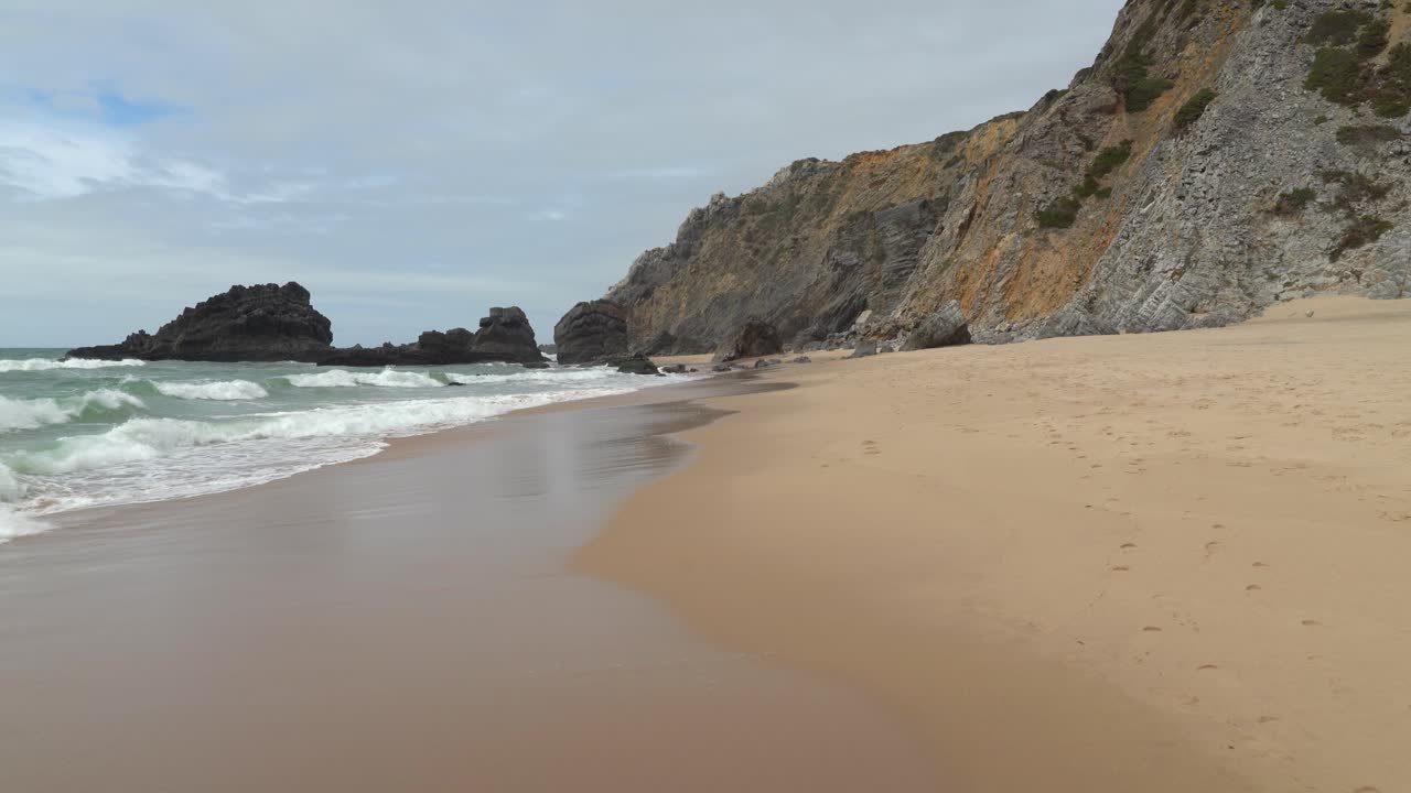 Ondas quebram na praia arenosa perto da Gruta da Adraga em Portugal