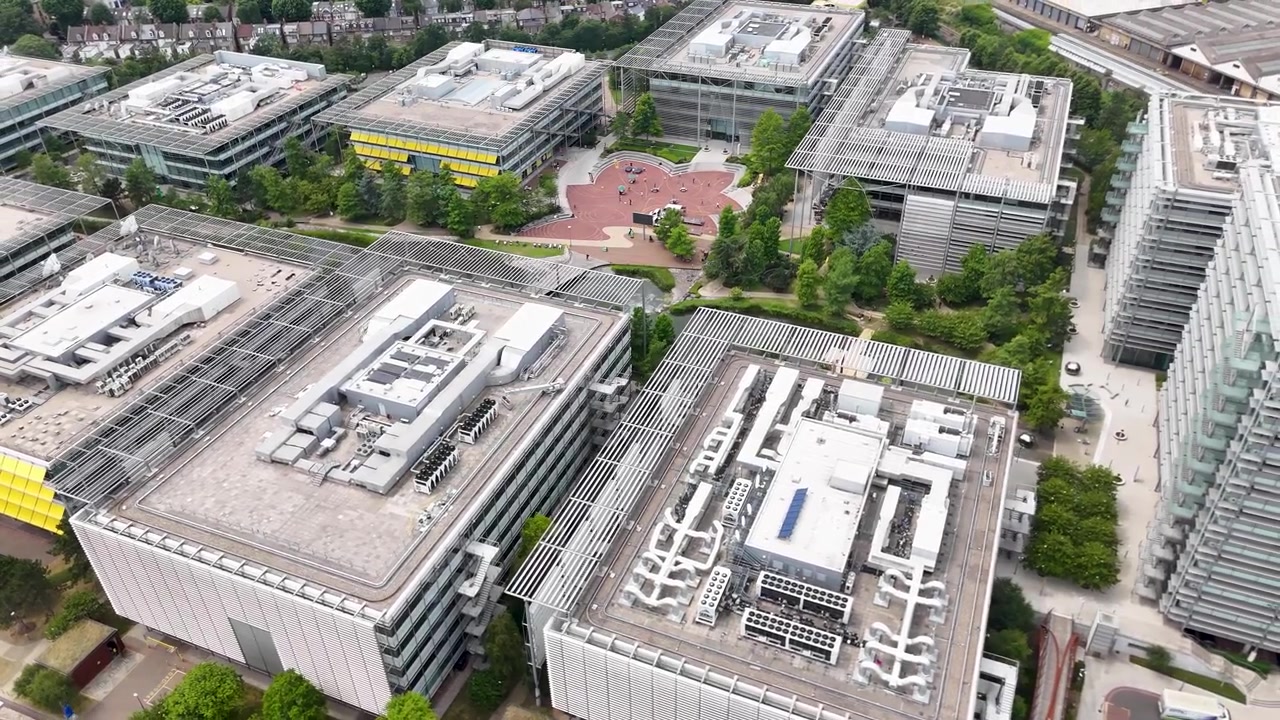 Vista cenital de los tejados de un moderno parque de oficinas, con salas de máquinas, lucernarios acristalados y terrazas sombreadas en amarillo