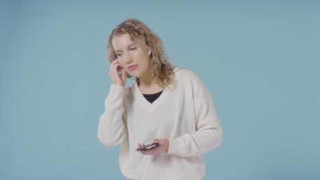 studio shot of young woman listening to music on mobile phone and dancing against blue background 2