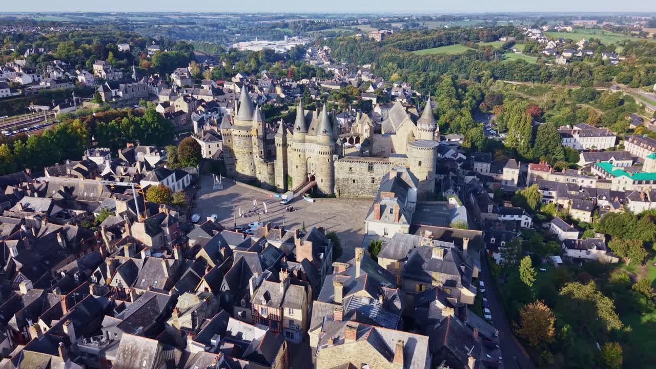 Drone flies forward above Vitré toward the sunlit castle façade, showing the town and countryside