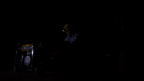 worker maintaining generator equipment in a dark, industrial setting