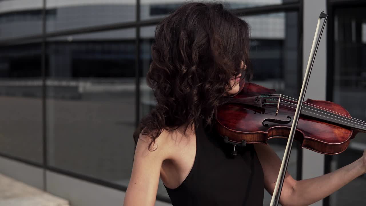 Close up of Elegant woman in black dress playing violin near glass building