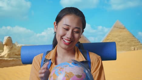 close up of asian female hiker with mountaineering backpack holding world globe in her hands and smiling while traveling in pyramid of giza