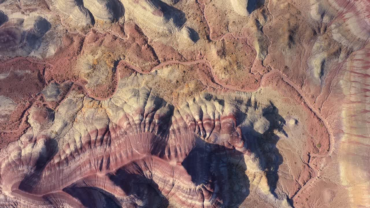 Rekaman drone dari atas ini menangkap detail rumit erosi geologis kuno. Lapisan sedimen berwarna-warni dan strata unik menciptakan pola abstrak yang kompleks
