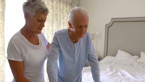 senior woman helping senior man to walk with walker in bedroom