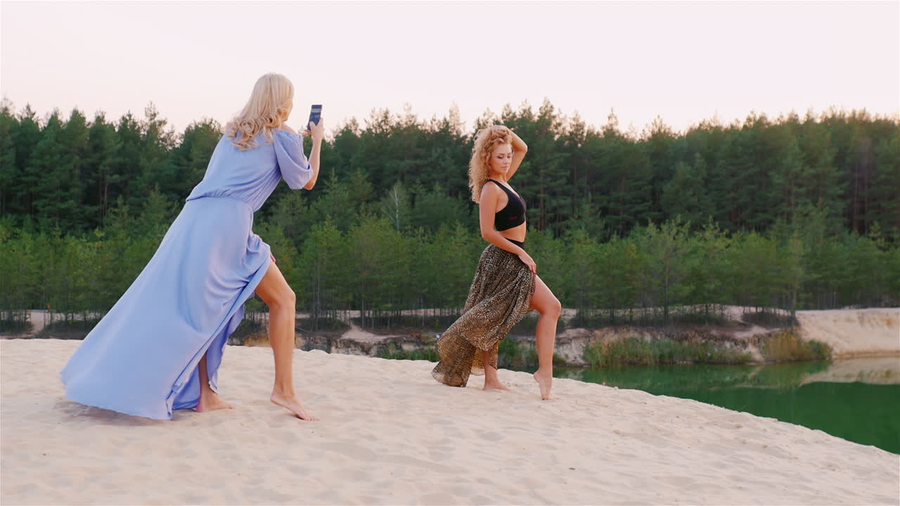 красивая женщина в платье позирует дьял своей подруге, которая фотографирует ее на телефон на фотографии