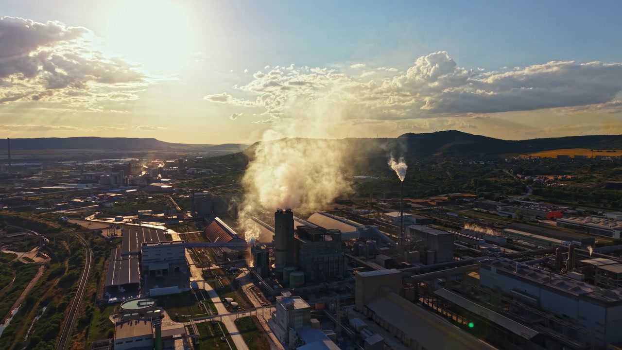 Le fabbriche operano e rilasciano fumo al tramonto in un'area industriale vicino a una catena montuosa durante l'ora d'oro