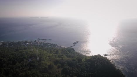 toma aérea de una pequeña isla con un pequeño pueblo y un embarcadero, rodeada por el océano azul por la tarde