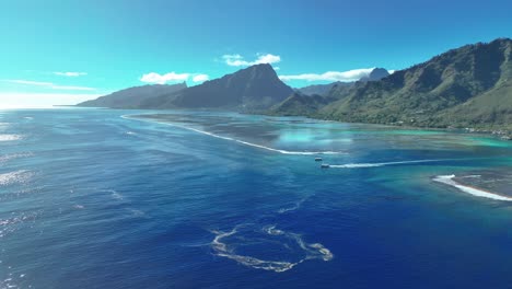 Aerial-View-Of-Boat-Sailing-Through-River-Canal-With-Forest-Mountains-In-The-Background-In-Moorea,-French-Polynesia