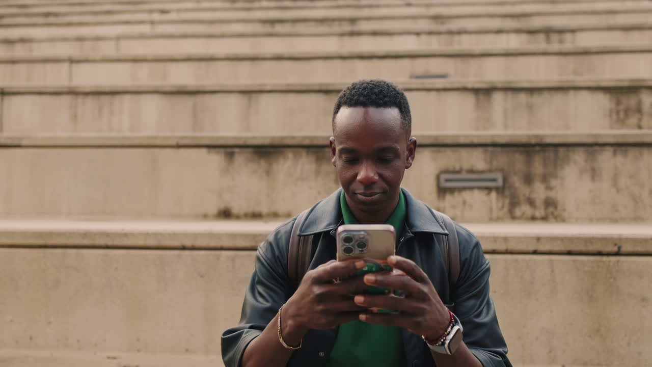 Giovane uomo di colore che usa lo smartphone mentre è seduto sui gradini