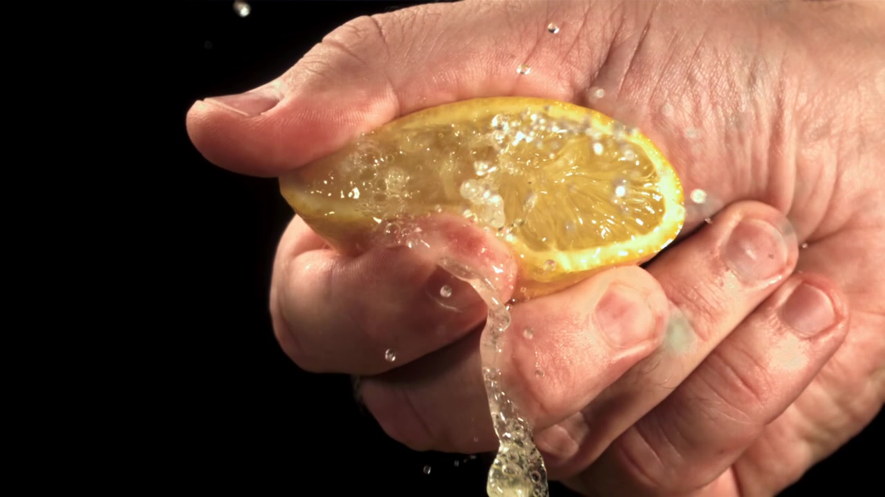 Cámara lenta de una mano exprimiendo medio limón con el jugo salpicando