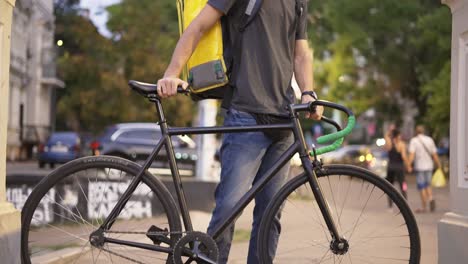 delivery man standing with bike and yellow bag in medical mask