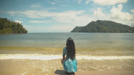 Sexy-female-squatting-on-a-jetty-with-the-waves-crashing-on-the-shore-with-mountains-in-the-background