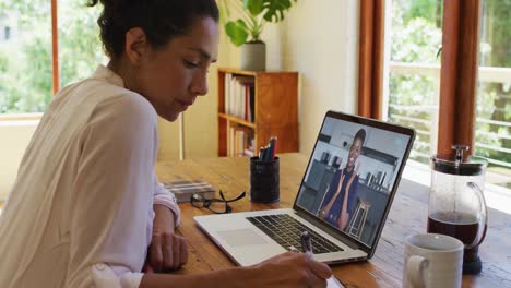 Mujer-Afroamericana-Tomando-Notas-Mientras-Realiza-Una-Videollamada-En-Una-Computadora-Portátil-En-Casa