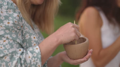 a young woman applies a pattern a drawing on a clay product with the help of tools sticks in a meadow in nature in an open space. a woman decorates a product in close-up.