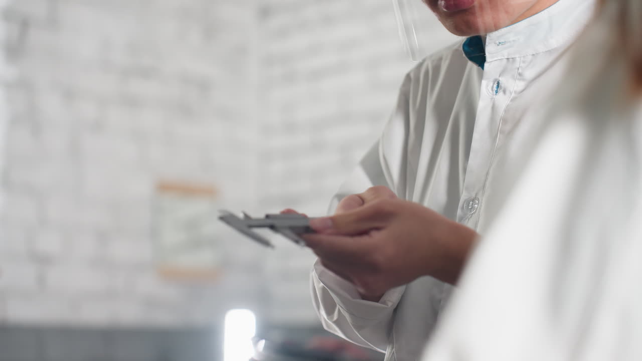 Nahaufnahme eines Labortechnikers in einer chinesischen Kfz-Werkstatt, konzentriert, während er aufgezeichnete Daten jemandem in der Nähe zeigt, trägt Schutzbrille und Laborkittel, beschäftigt mit Präzisionsarbeit