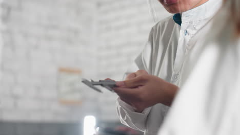 primer plano de un técnico de laboratorio en un taller automotriz chino, enfocado mientras muestra datos grabados a alguien cercano, con gafas de protección y bata de laboratorio, involucrado en un trabajo de precisión