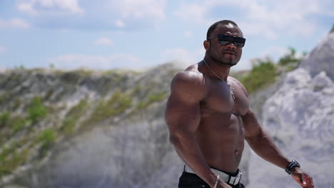 waist up portrait view of the athletic naked man wearing glasses walking outside and showing his naked torso. man posing at the sandy beach