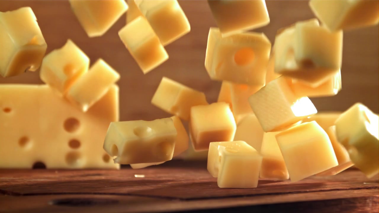 Deliziosi cubetti di formaggio che cadono al rallentatore sul legno.
