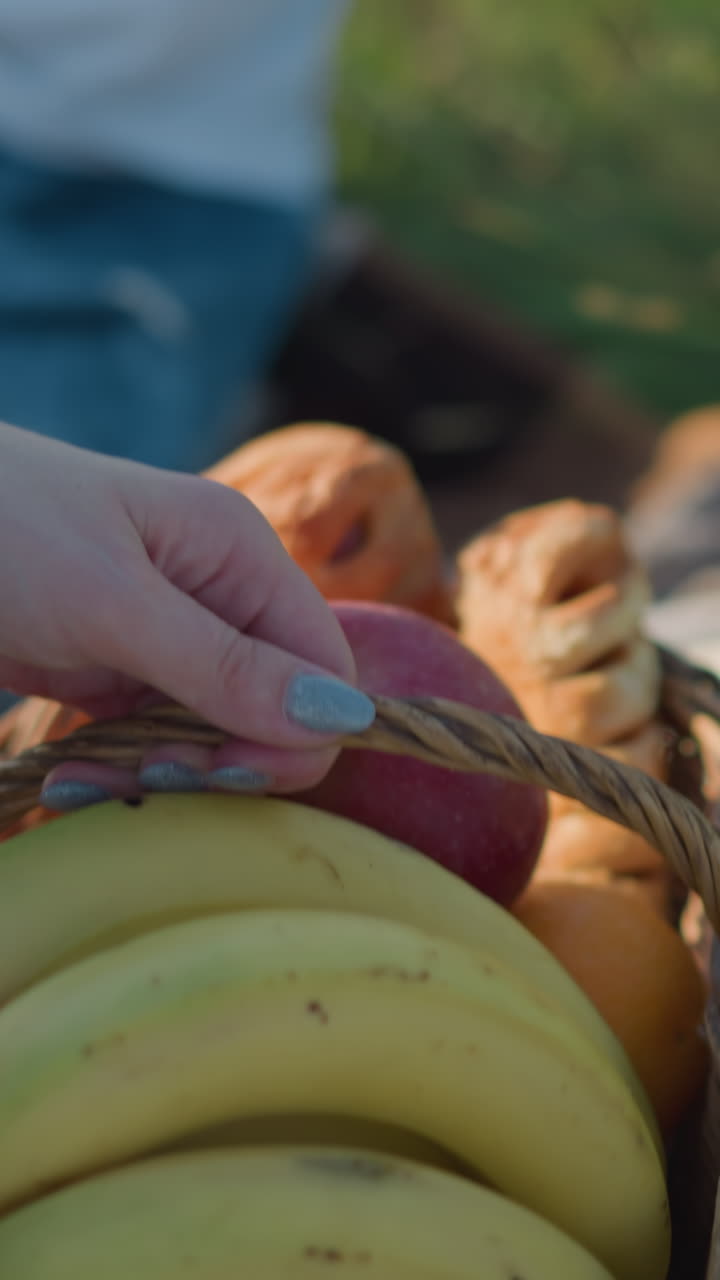 바나나, 사과 및 다른 과일로 가득 찬 바구니를 체크 된 피크닉 담요 위에 놓은 여자의 클로즈업.