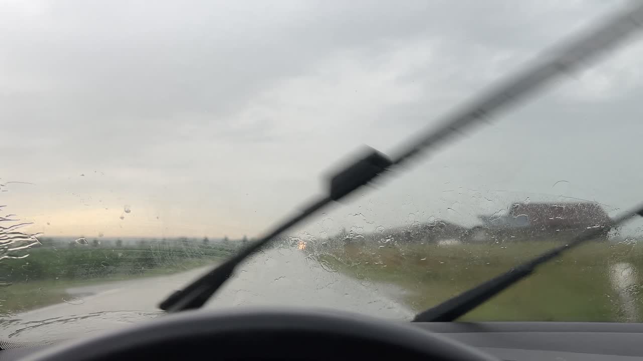 Pioggia battente con tergicristalli in funzione su una strada rurale in Baviera. Vista attraverso il parabrezza dell'auto durante il movimento dei tergicristalli e scarsa visibilità sotto un cielo nuvoloso